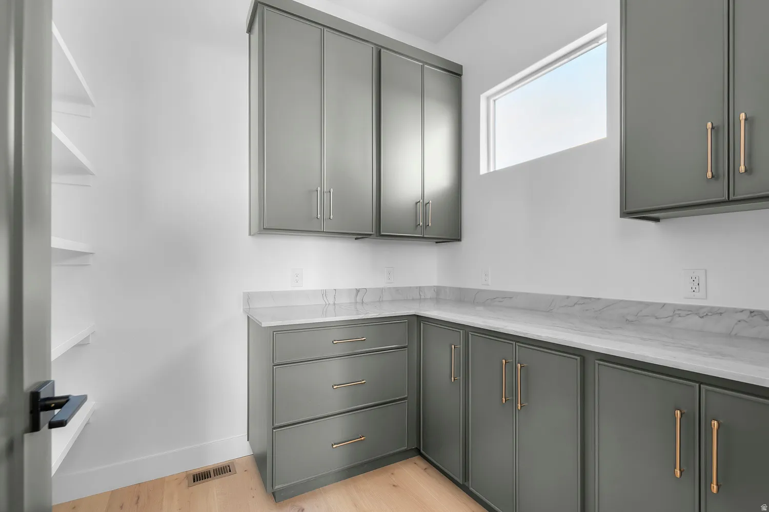 Bright utility space featuring grey cabinetry with gold-tone hardware, white countertops, and light wood-finish flooring