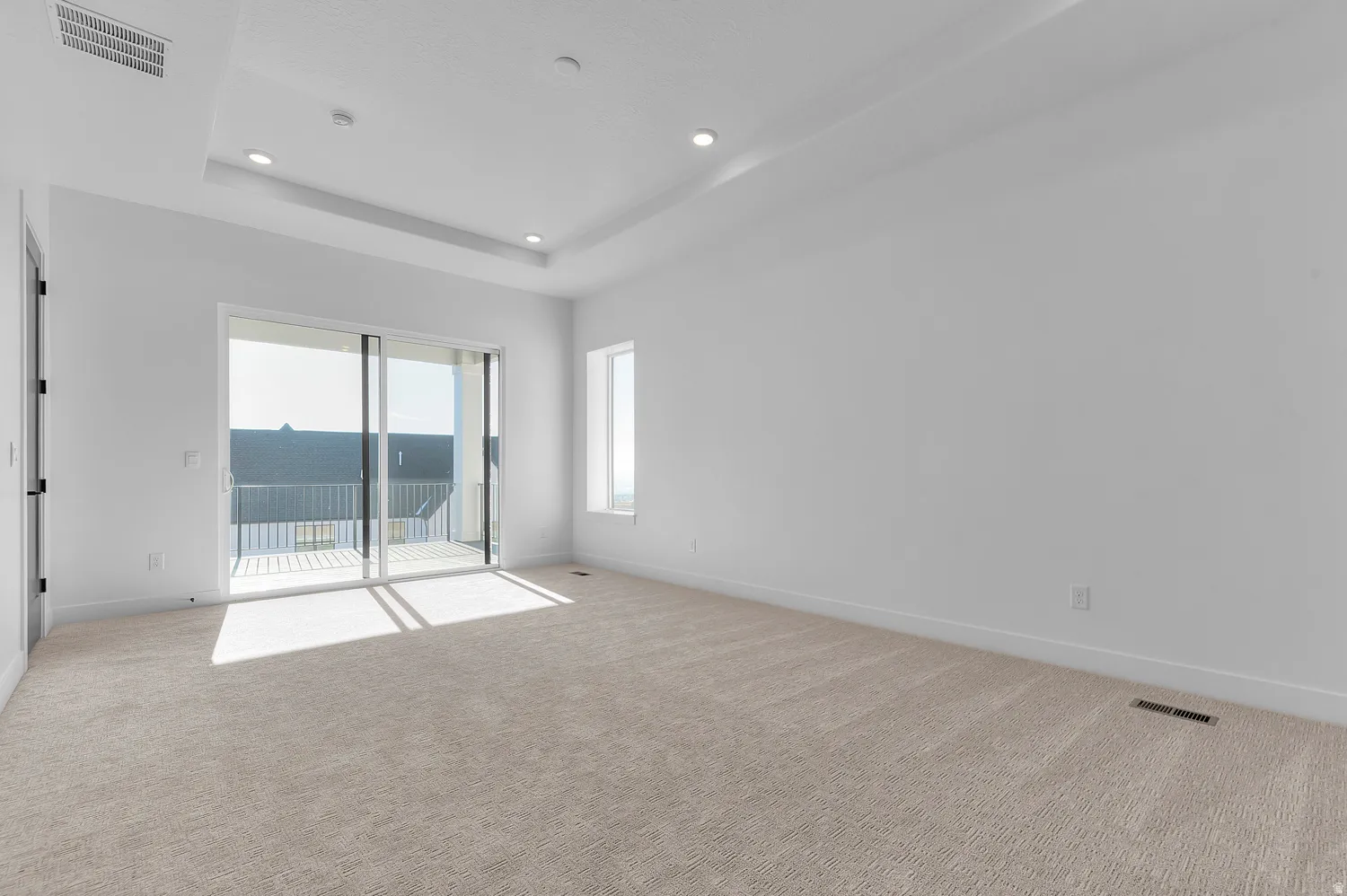 Spacious room featuring light-colored carpeting, a tray ceiling with recessed lighting, and a private balcony accessed through sliding glass doors