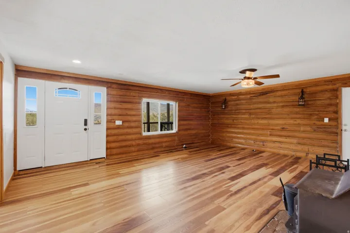 Spacious interior featuring wood-finish flooring, log-style wall paneling, and a bright white entry door with clear glass sidelights