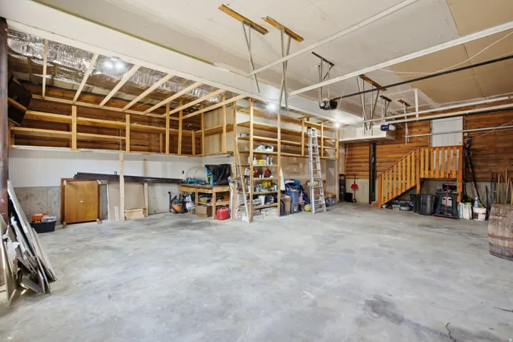 Spacious garage featuring a concrete floor, built-in wooden shelving, exposed wood beam ceiling, and wood-paneled walls