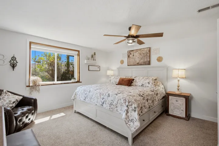 Bedroom featuring a large window with wood trim, neutral carpeting, and a ceiling fan with integrated lighting