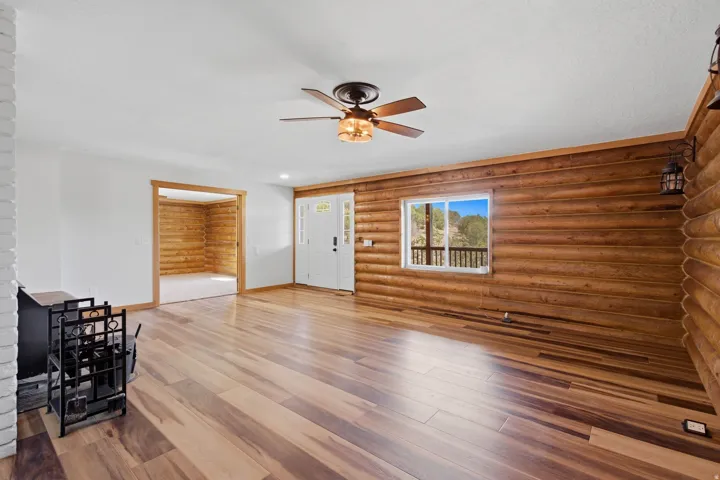 Spacious room featuring wood-finish flooring, a white entry door, and a prominent log wall with sconce lighting