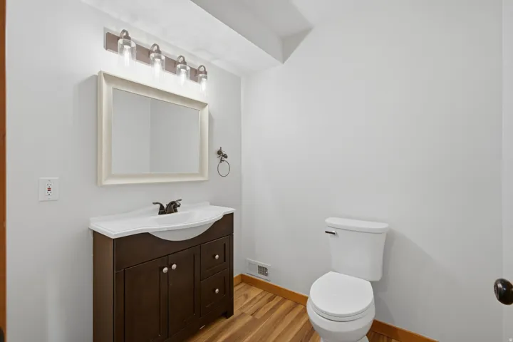 Contemporary bathroom featuring a dark wood-finish vanity with a white integrated sink, a framed mirror, and a four-light vanity fixture