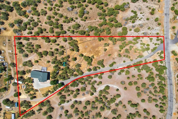 Expansive aerial view showcasing a large land parcel with natural foliage and a single-story residence featuring a dark green roof