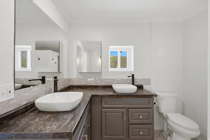 Bathroom featuring a dual-sink vanity with vessel sinks, dark countertops, and a gray shaker-style cabinet