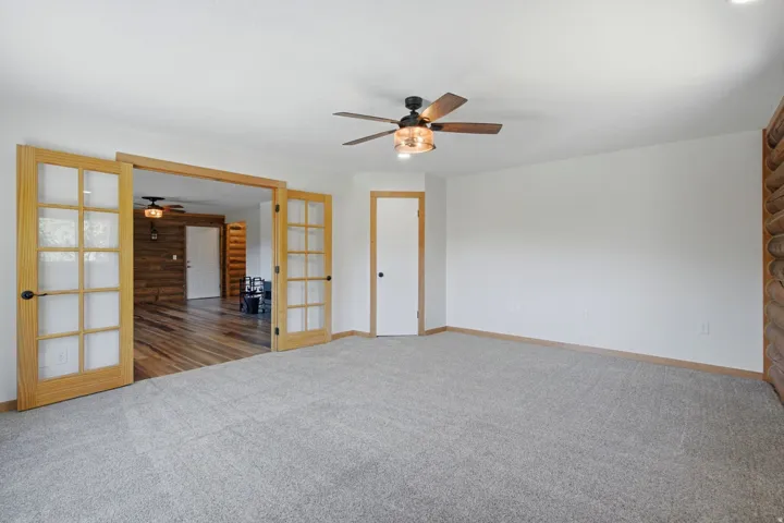 Expansive room with neutral carpeting and a ceiling fan