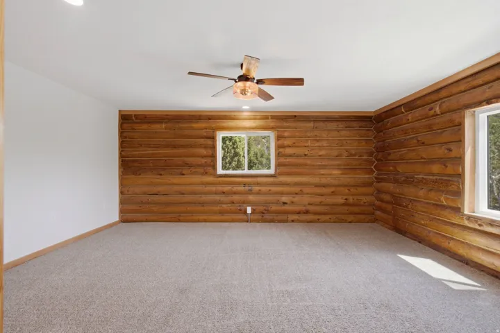 Room featuring log wood accent walls, white painted walls, and light-colored carpet flooring