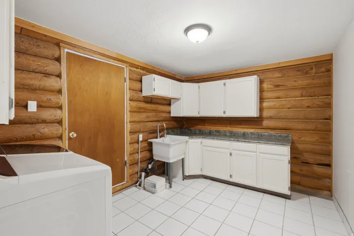 Laundry room featuring log-style wood paneling, white tile flooring, white cabinetry, a utility sink, and a laminate countertop