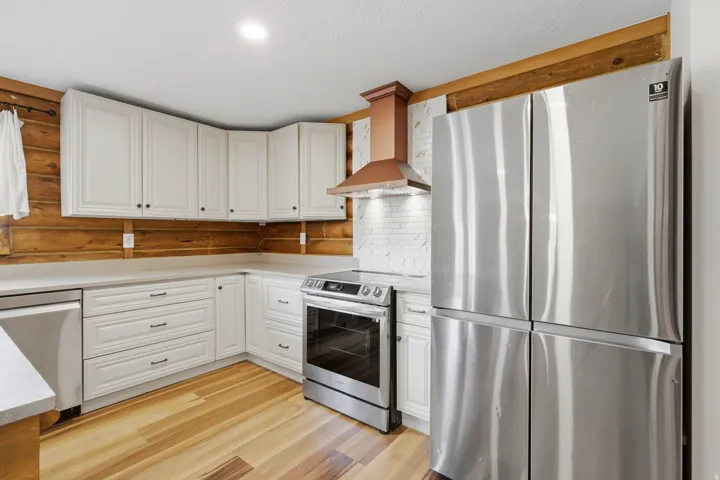 Kitchen featuring white cabinetry, light countertops, wood-finish flooring, and a stainless steel refrigerator