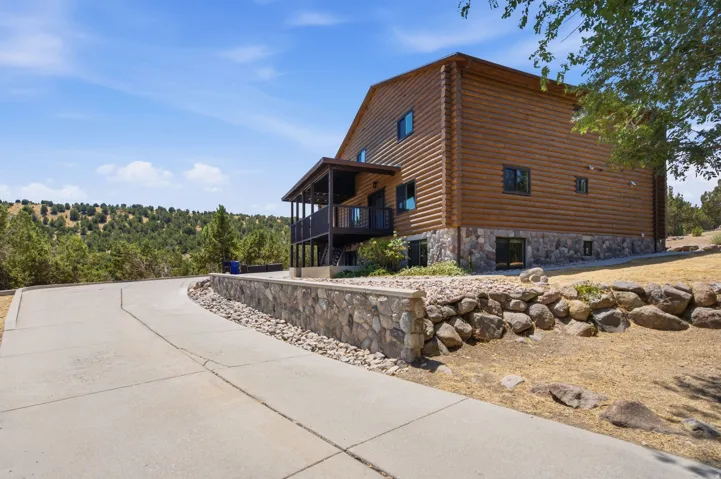 Rustic log exterior with stone foundation, featuring a concrete driveway and an upper-level covered balcony