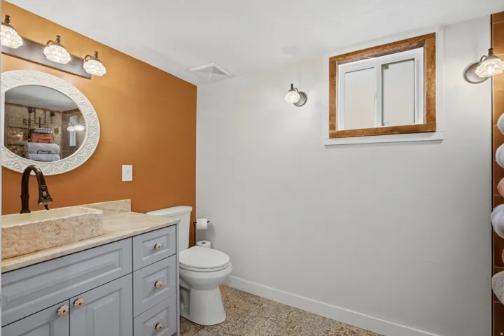 Bathroom featuring a stone vessel sink, light gray vanity with decorative hardware, and a round framed mirror