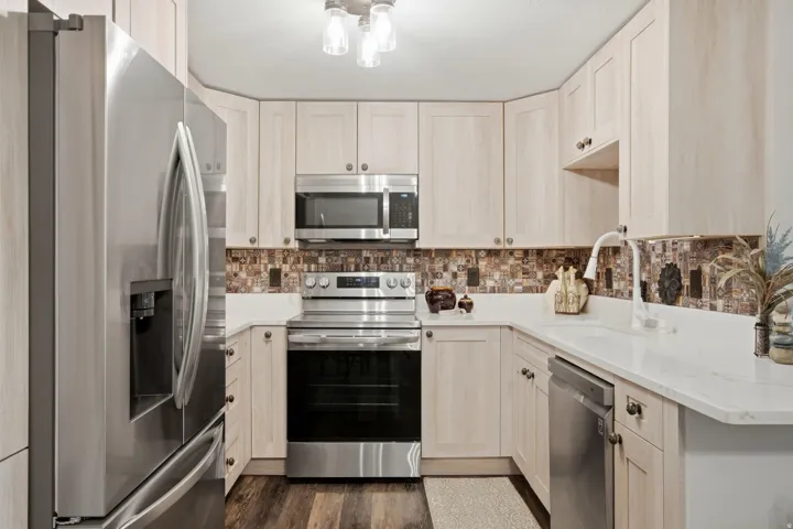 Kitchen featuring light wood-finish cabinetry, stainless steel appliances, white countertops, and an intricate tile backsplash