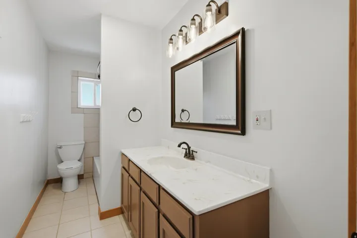 Bathroom featuring a dual-sink vanity with a light-toned countertop, wood-finish cabinetry, and an ornate framed mirror