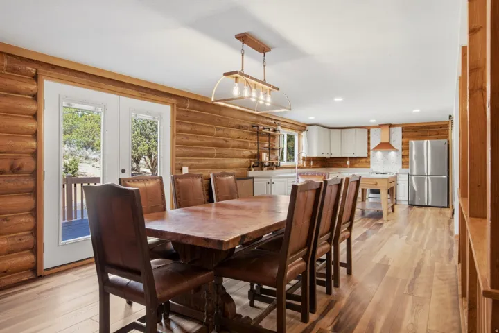 Open-concept living space with log walls, light wood-finish flooring, white double French doors, a kitchen featuring white cabinetry, and stainless steel appliances
