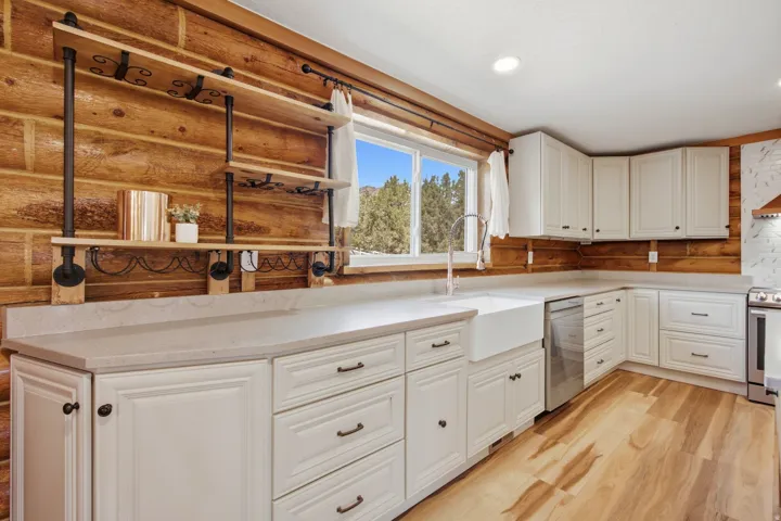 Kitchen featuring wood-finish flooring, white cabinetry, a farmhouse sink, light-toned countertops, and a window framing a natural landscape