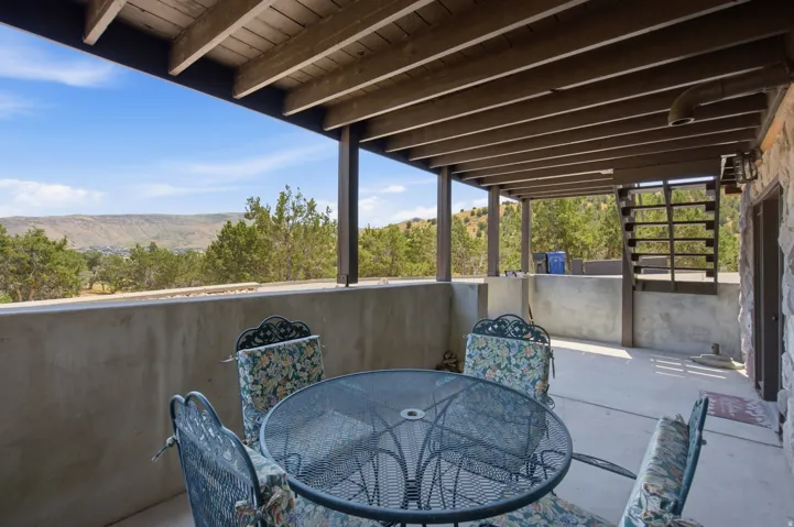 Covered outdoor living space featuring concrete flooring, a natural wood beam ceiling, and a stone exterior wall