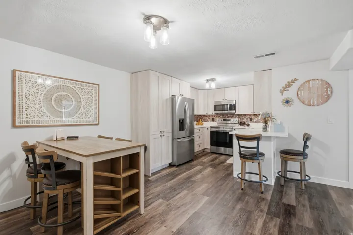 Modern kitchen featuring light wood-finish cabinetry, stainless steel appliances, a tiled backsplash, and wood-finish flooring