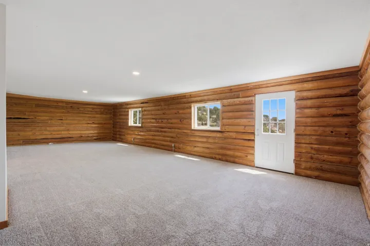 Spacious room featuring log-style wood walls, light grey carpeting, and recessed ceiling lighting