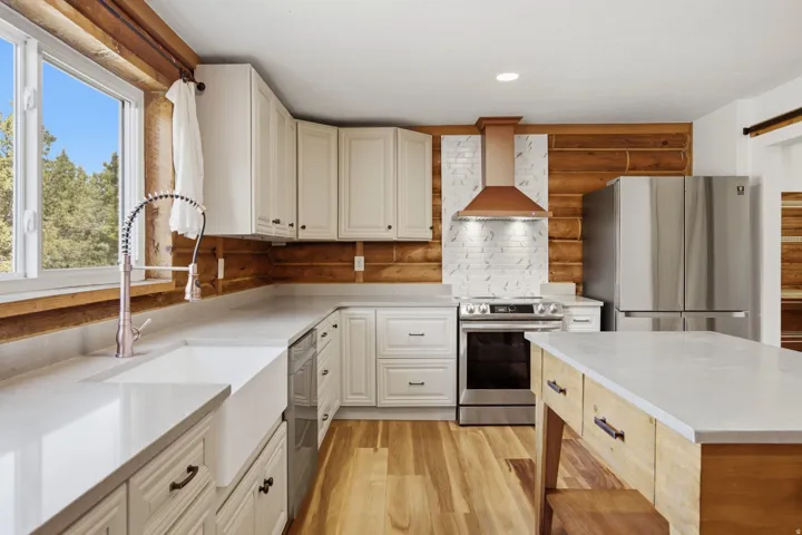 Kitchen featuring wood-finish flooring, white cabinetry, a farmhouse sink with a gooseneck faucet, light-toned countertops, and a wood-paneled accent wall