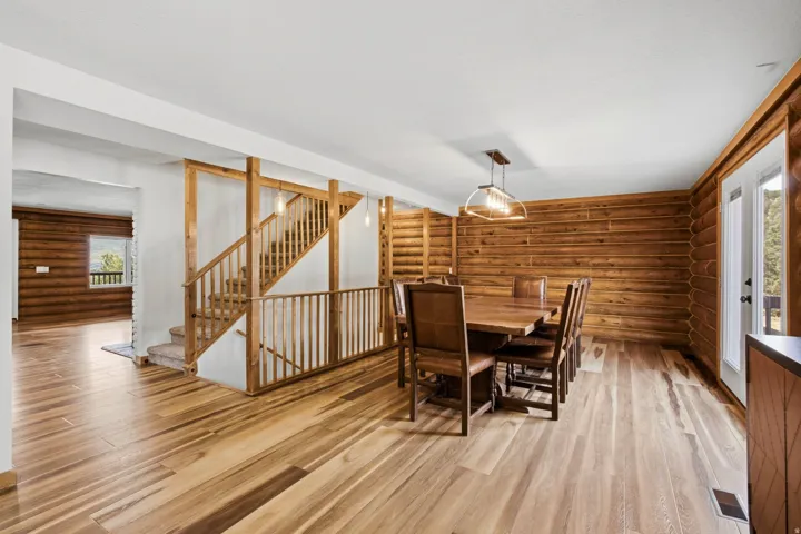 Spacious interior featuring wide plank wood-finish flooring, log-style wall finishes, a prominent wooden staircase with carpeted treads, and a glass-paneled exterior door