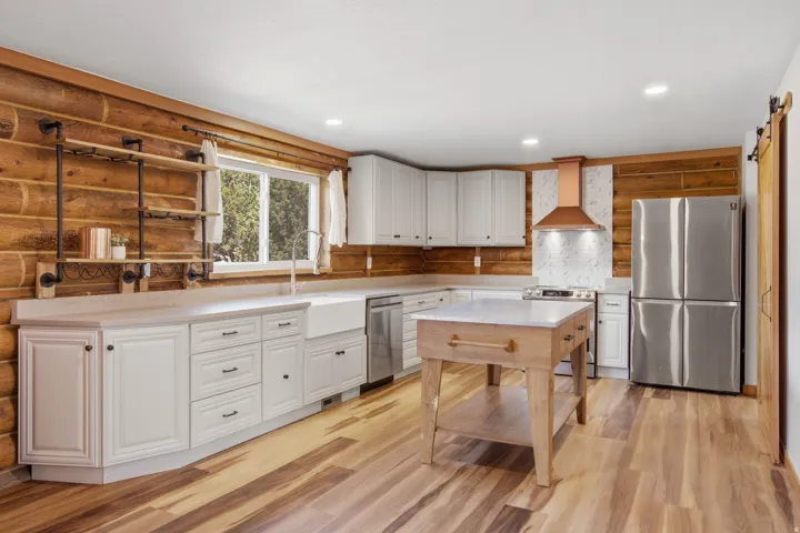 Kitchen featuring log walls, white cabinetry, wood-finish flooring, a farmhouse sink, and a copper range hood