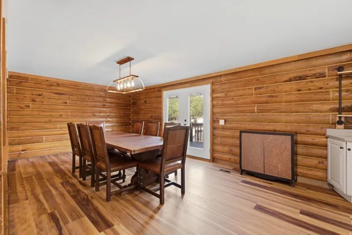 Dining area featuring wood-finish flooring, log-style wall paneling, and a contemporary chandelier