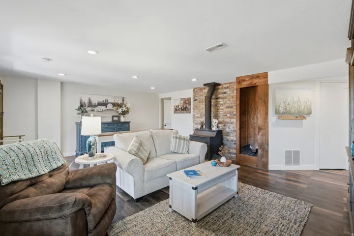 Living area featuring wood-finish flooring, recessed lighting, and a brick accent wall with a wood-burning stove