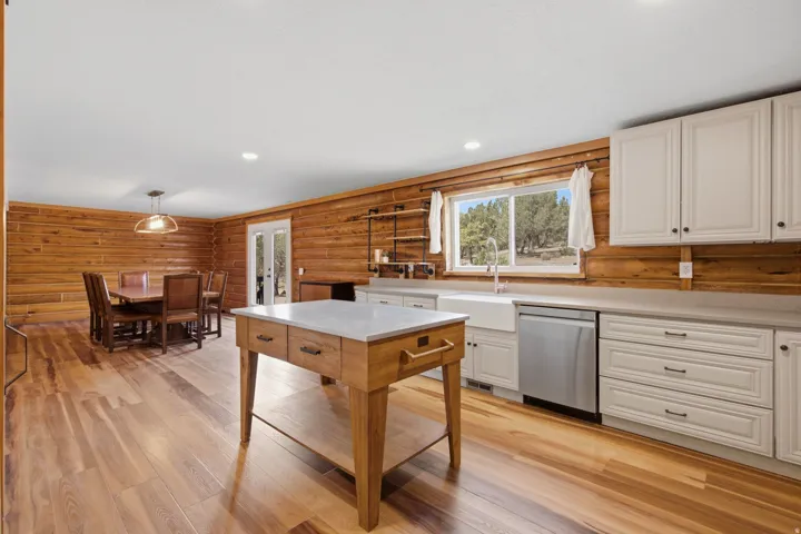 Open-concept kitchen and dining area featuring wood-finish flooring, wood paneling, white shaker-style cabinetry, and a large farmhouse sink