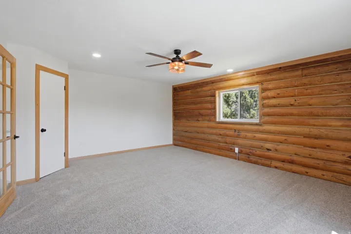 Room featuring a natural wood log wall, neutral carpet flooring, recessed lighting, and a ceiling fan