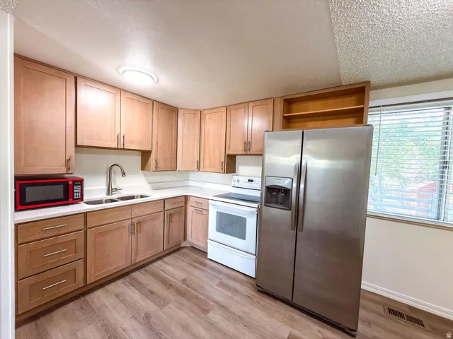 Kitchen featuring wood-finish flooring, light wood cabinetry, white countertops, and a double basin stainless steel sink with a gooseneck faucet