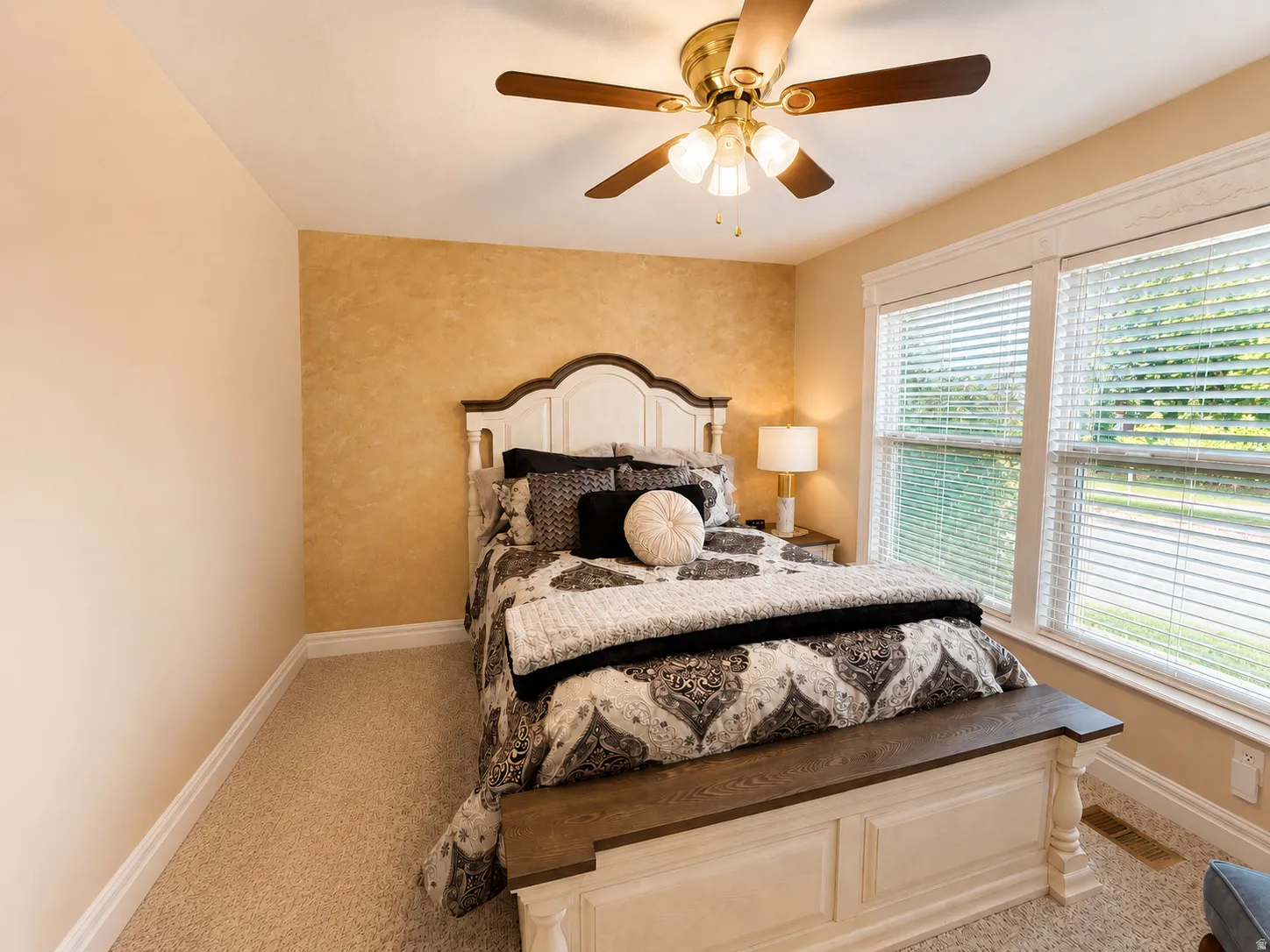 Carpeted bedroom featuring a decorative accent wall, ceiling fan with integrated lighting, and two large windows with blinds