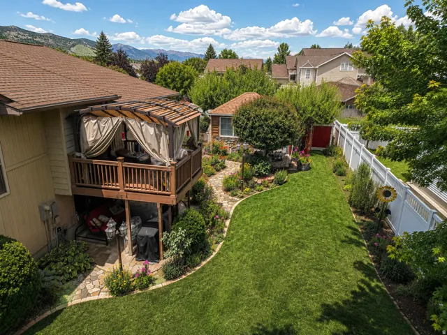 Terraced backyard featuring a wooden deck with a slatted pergola and privacy drapes, a stone patio, and a manicured lawn