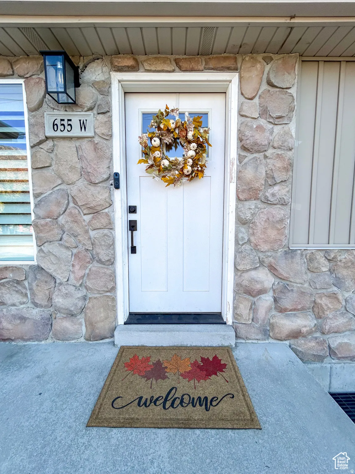 Stone facade with a white front door featuring upper window lites, a black exterior sconce, and a visible address plaque