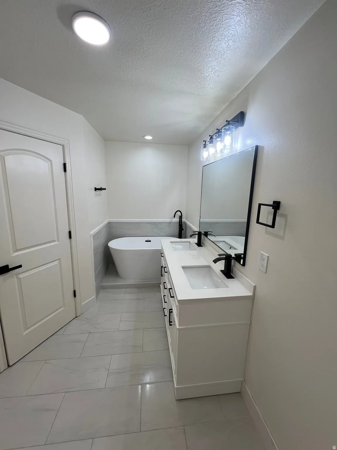 Contemporary bathroom featuring a freestanding soaking tub, a double vanity with integrated sinks, matte black fixtures, and large format tile flooring