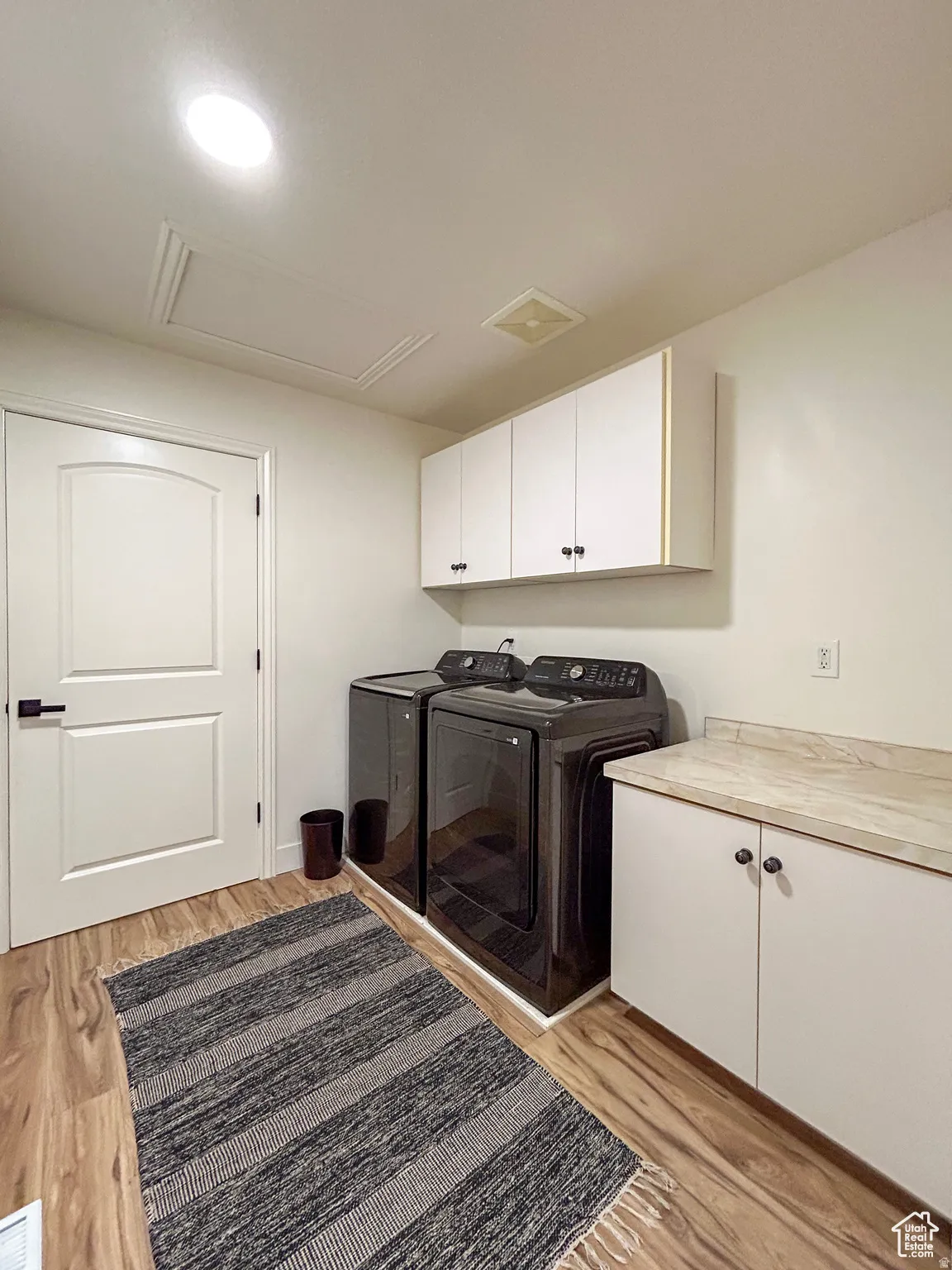 Laundry area featuring wood-finish flooring, white cabinetry with dark hardware, and a light-toned countertop