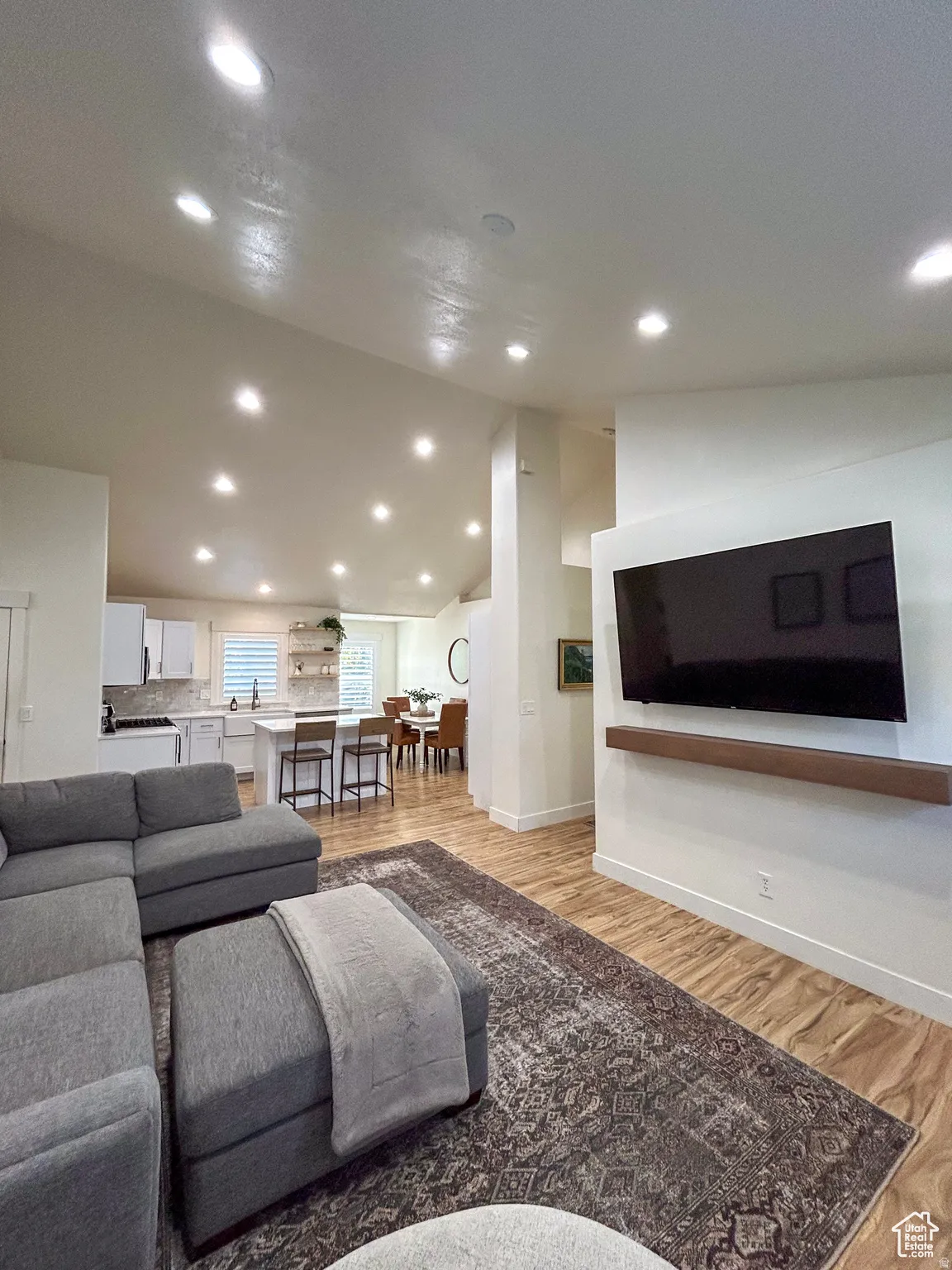Vaulted ceilings with recessed lighting illuminate an open-concept living area featuring wood-finish flooring