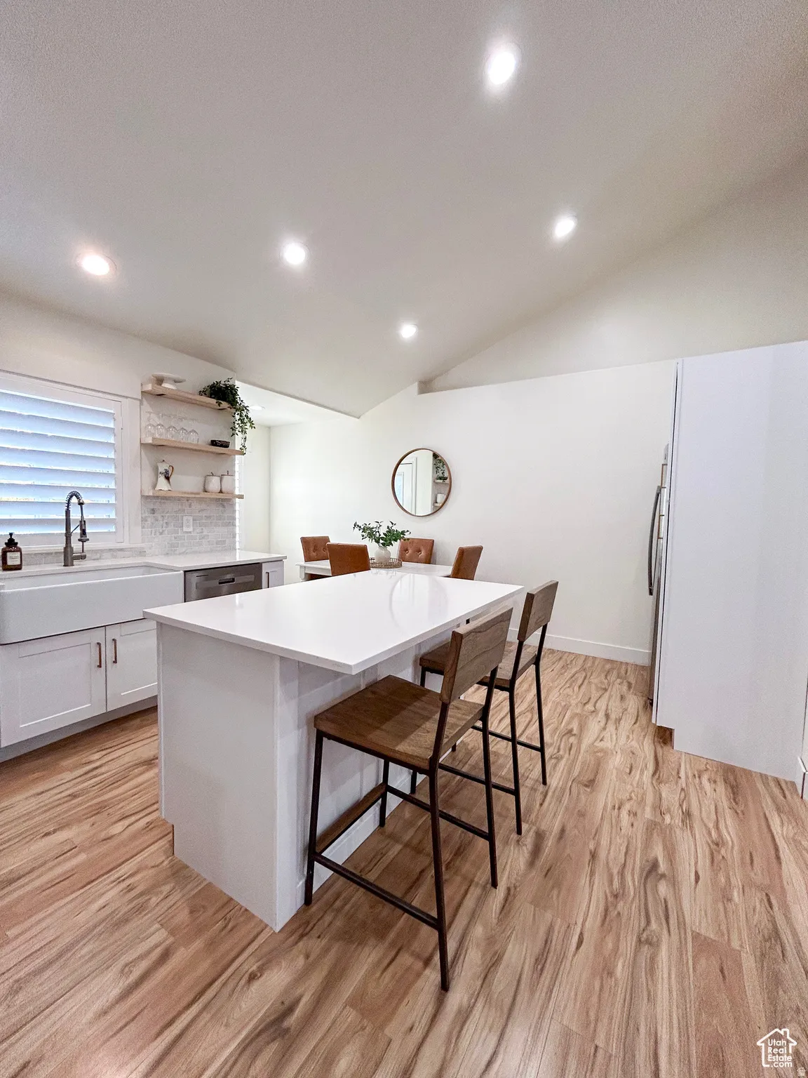 Spacious kitchen featuring an expansive central island with seating, white shaker cabinetry, and wood-finish flooring