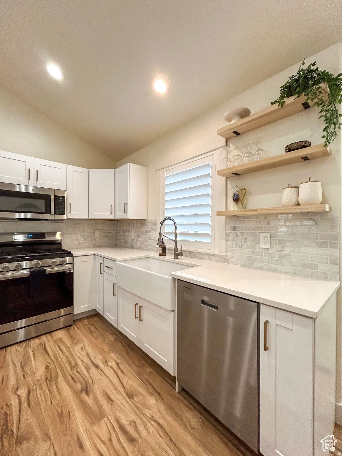 Modern kitchen featuring white shaker cabinetry, stainless steel appliances, a farmhouse sink, and light wood-finish flooring