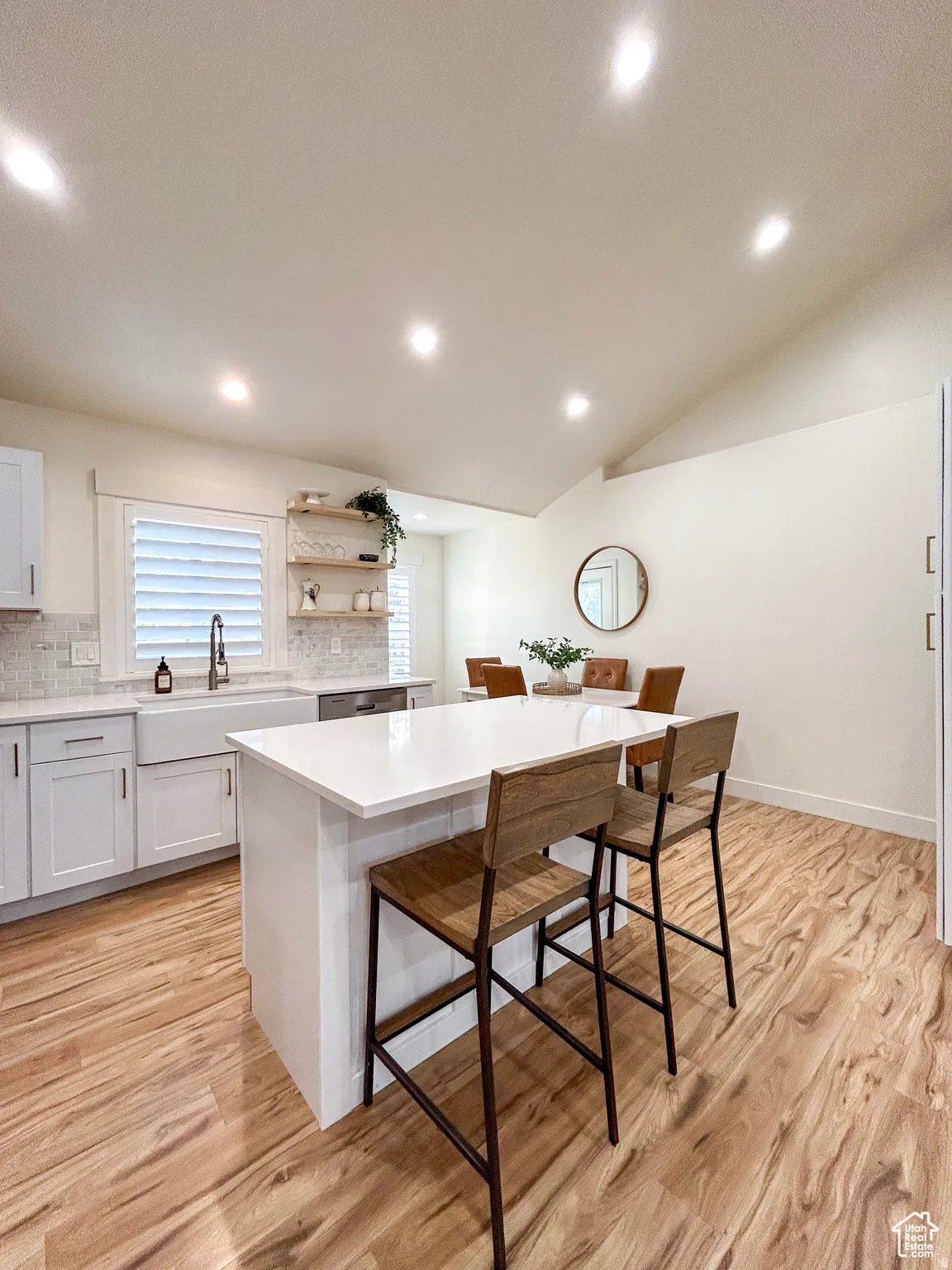 Kitchen featuring a white island with a solid surface countertop, wood-finish flooring, white cabinetry, a farmhouse sink, and a tiled backsplash
