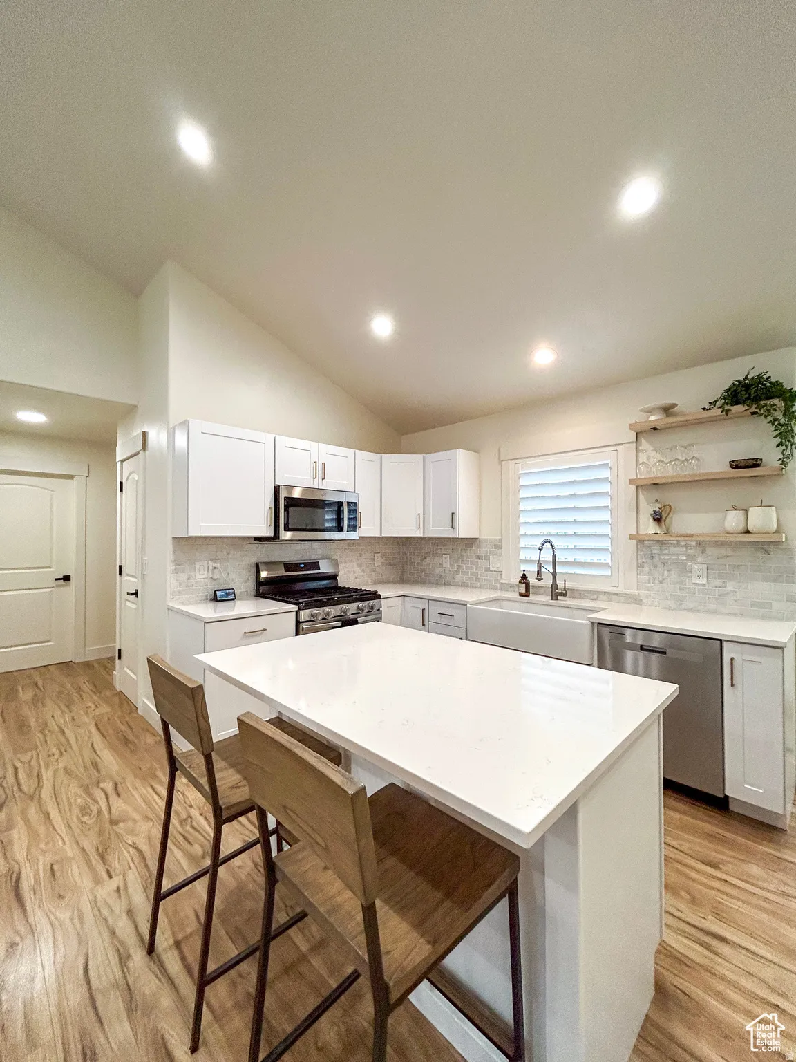 Kitchen featuring vaulted ceiling with recessed lighting, white shaker cabinetry, stainless steel appliances, a farmhouse sink, and wood-finish flooring