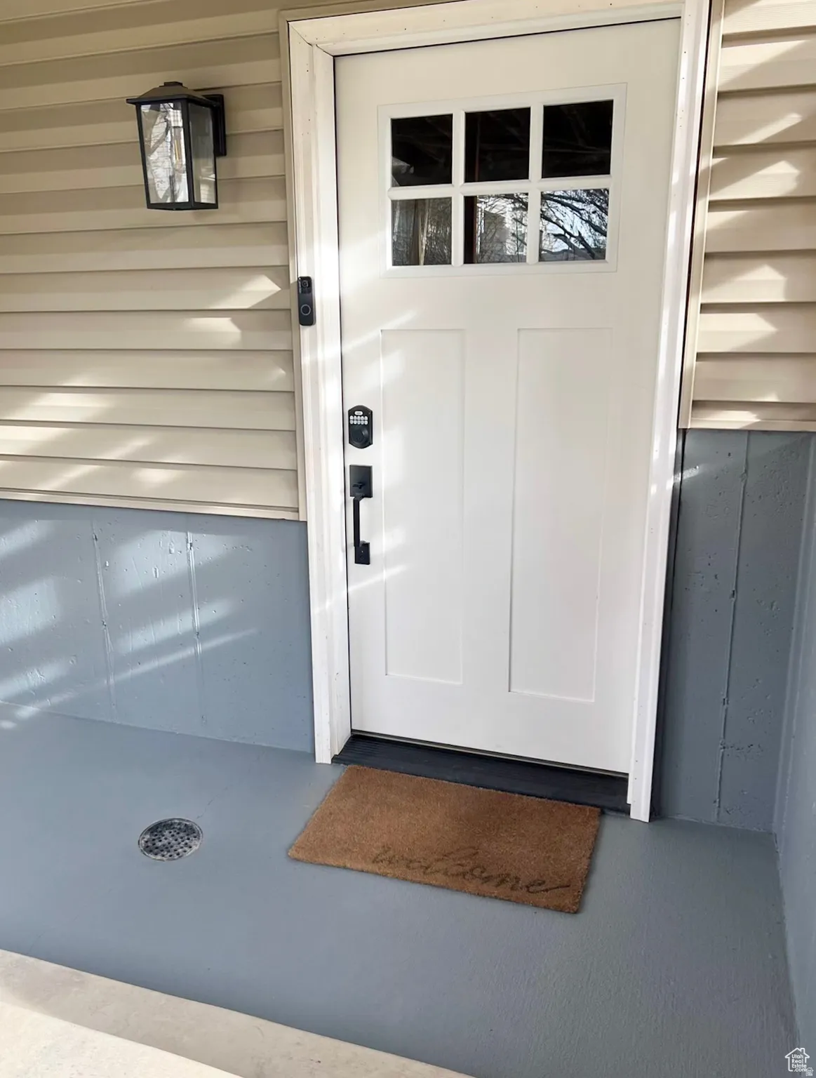 Entryway featuring a white paneled door with divided lite glass, black hardware, an overhead wall sconce, and horizontal siding