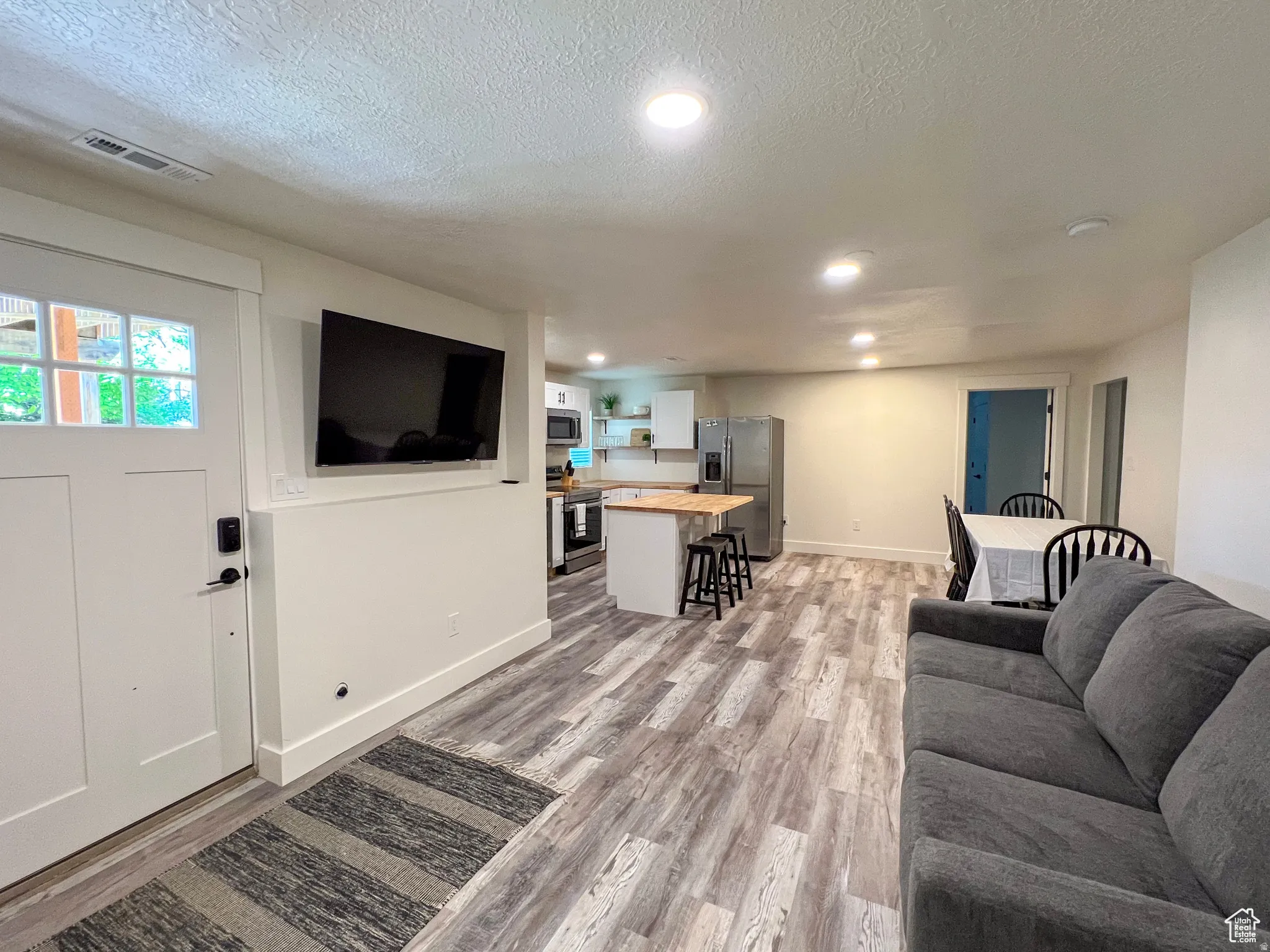 Open-concept living space featuring wood-finish flooring, recessed lighting, and a modern kitchen with a butcher block island