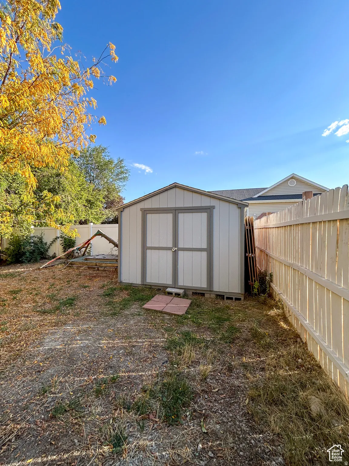 Backyard featuring a white storage shed with double doors, wood fencing, and mature trees