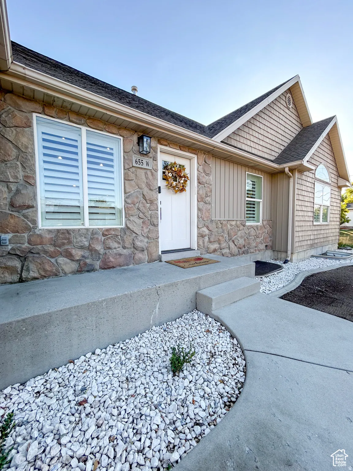 Stone veneer and horizontal siding exterior featuring a white entry door with an overhead lantern sconce