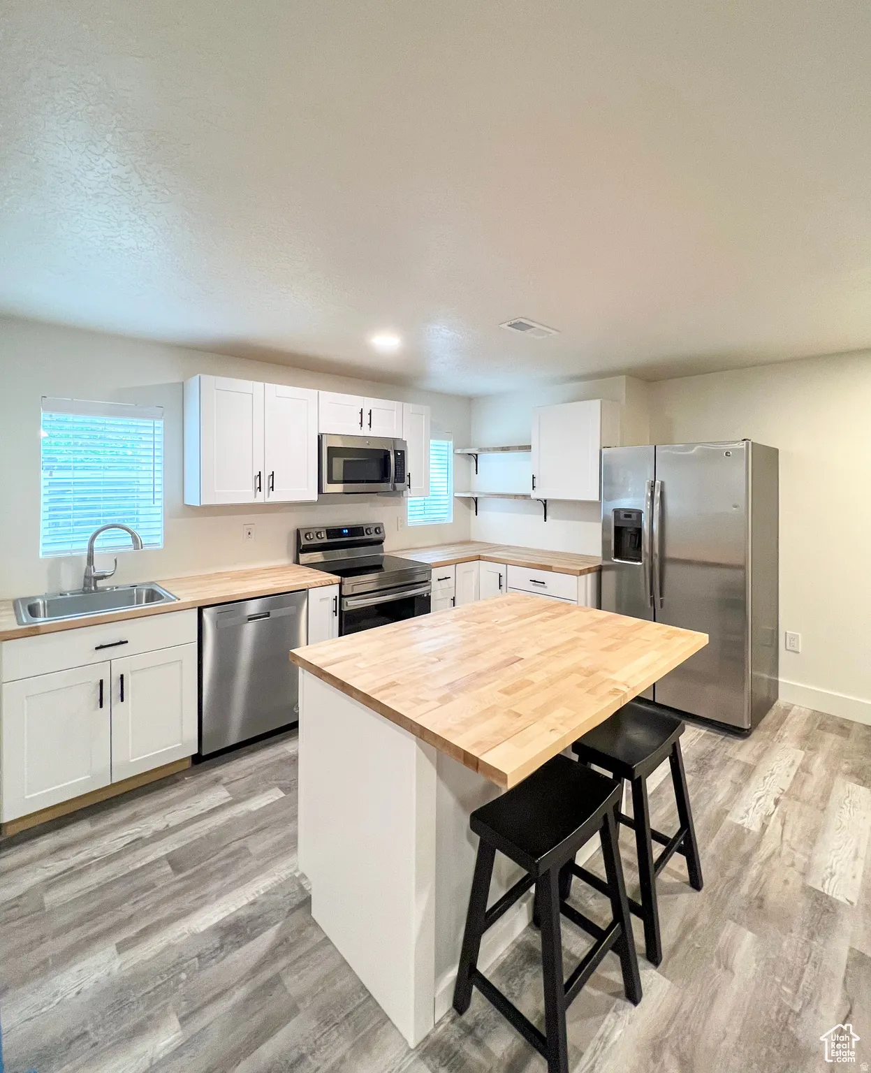 Modern kitchen featuring white cabinetry, butcher block countertops, stainless steel appliances, and wood-finish flooring