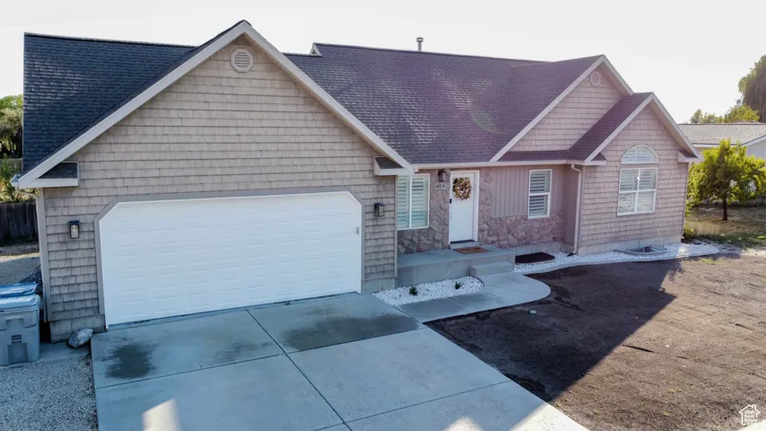 Exterior featuring cedar shake siding, stone accents, a dark shingle roof, an arched window, and a white garage door with exterior lighting fixtures