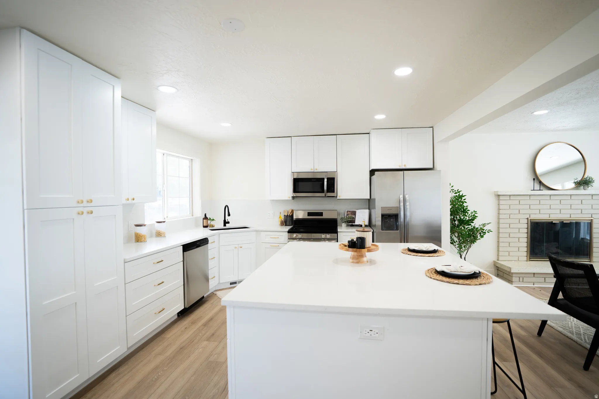 Modern kitchen featuring white shaker cabinetry, stainless steel appliances, a center island with countertop seating, recessed lighting, and wood-finish flooring