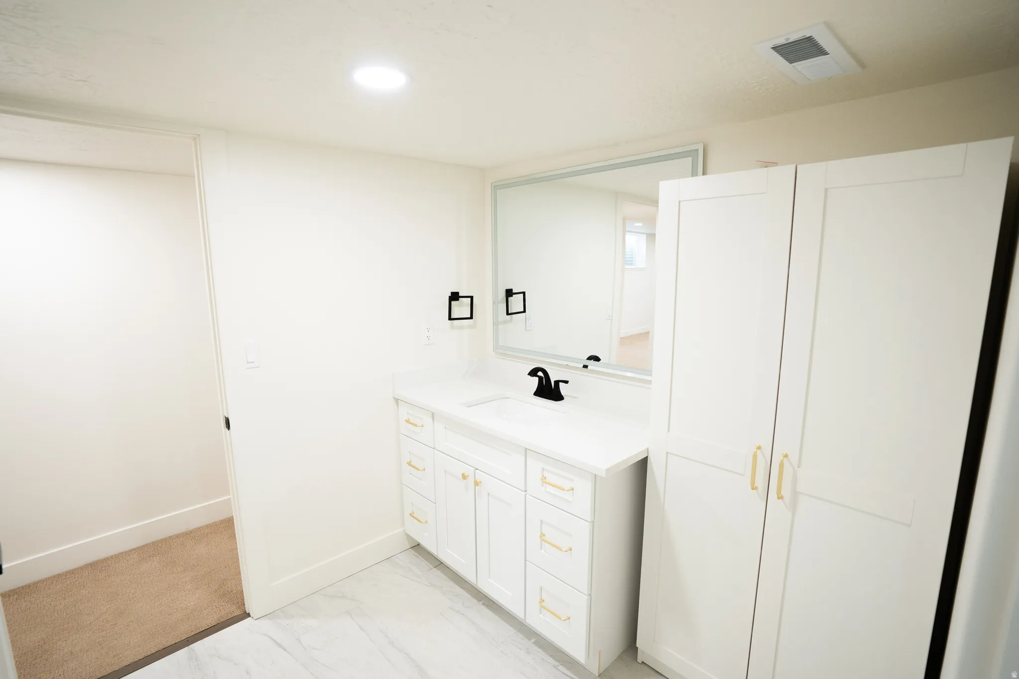 Bathroom vanity featuring a white countertop, undermount sink, and matte black faucet