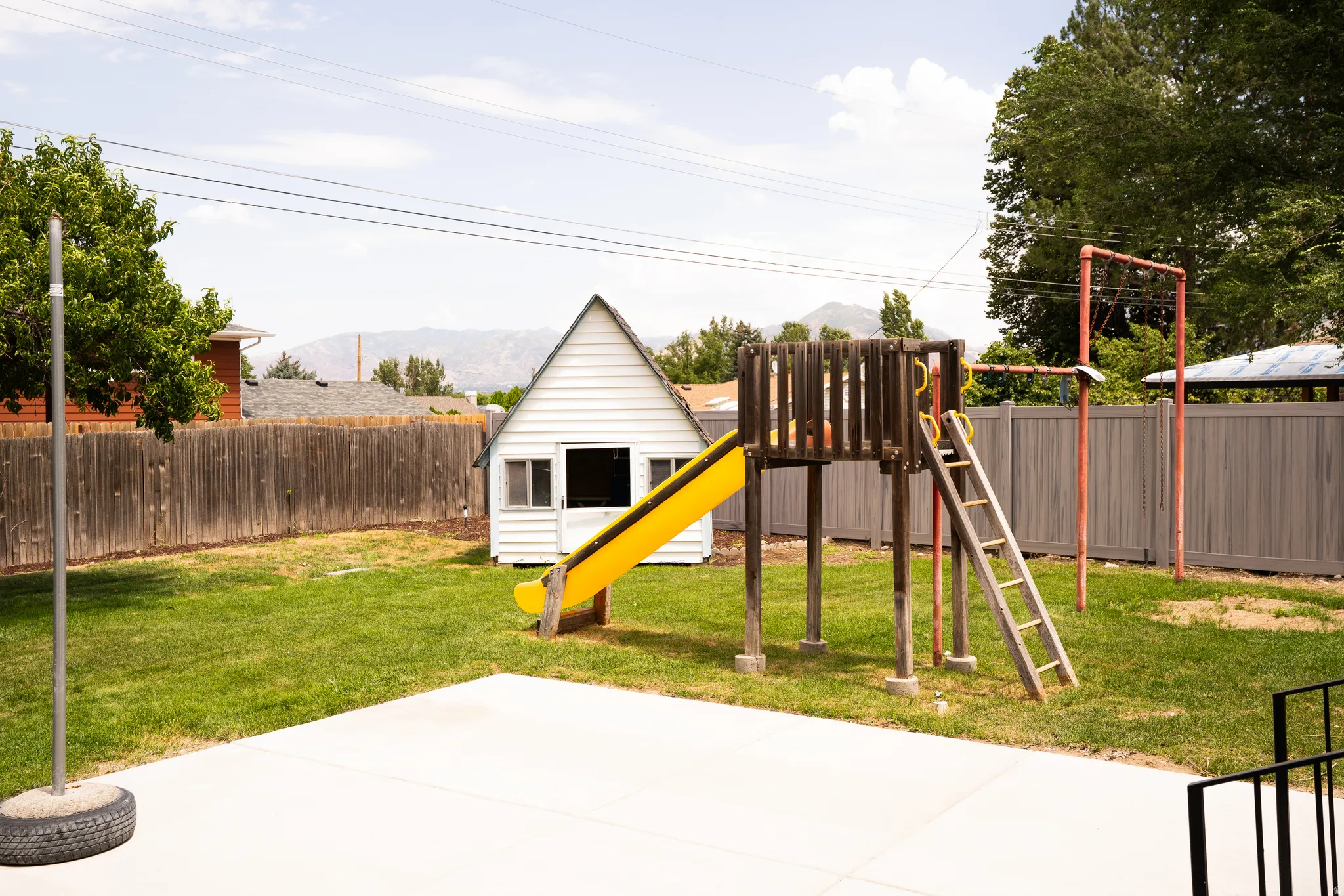 Expansive backyard featuring a concrete patio, mature trees, and a full perimeter fence