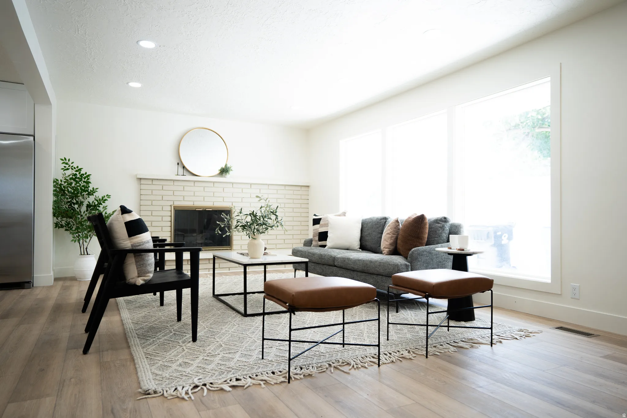 Spacious living area featuring light wood-finish flooring, recessed lighting, and a white brick fireplace with a mantel